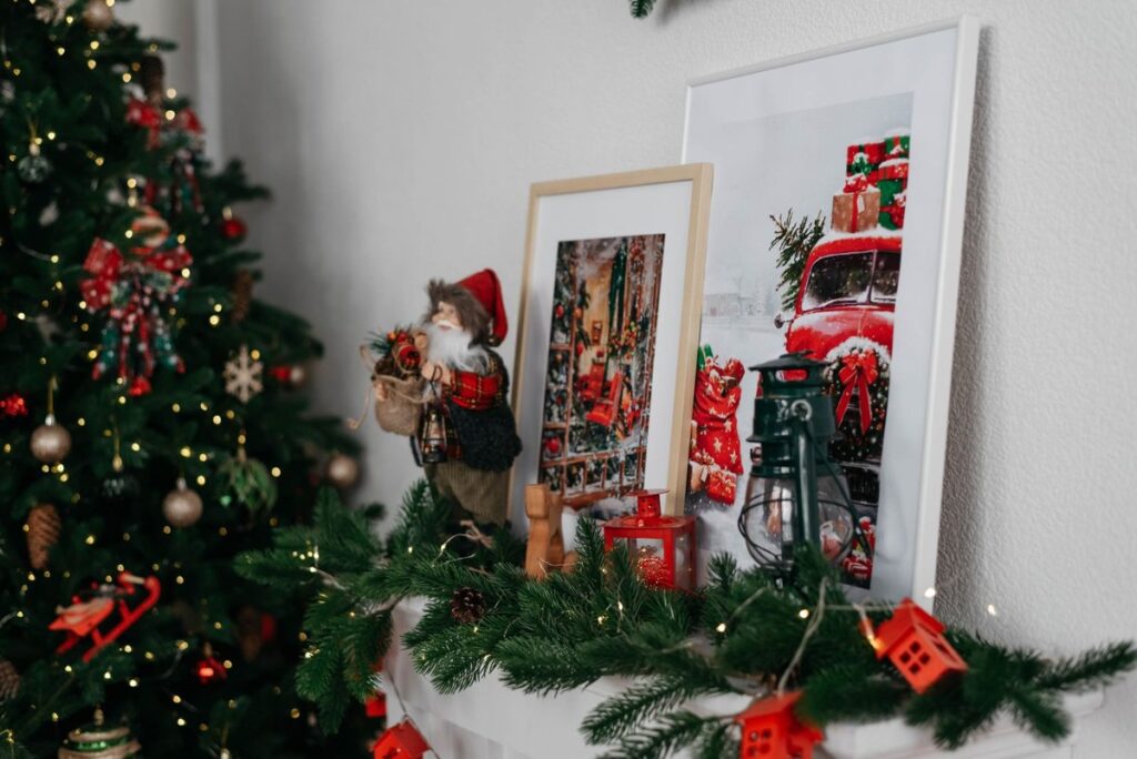 Christmas mantel decorated with evergreen garland, framed art and a tree