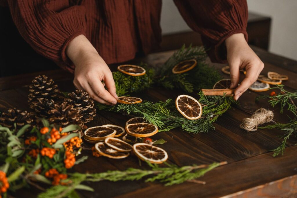Hands making a Christmas wreath with dried oranges, pinecones and greenery