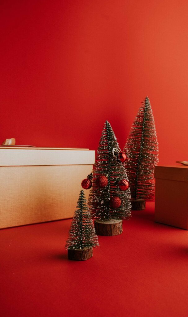 Small Christmas trees between gold gift boxes on a red background