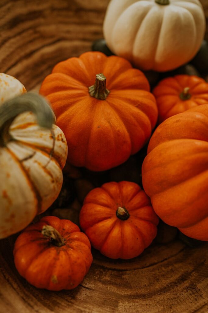 Assorted small orange and white pumpkins piled in a wooden bowl