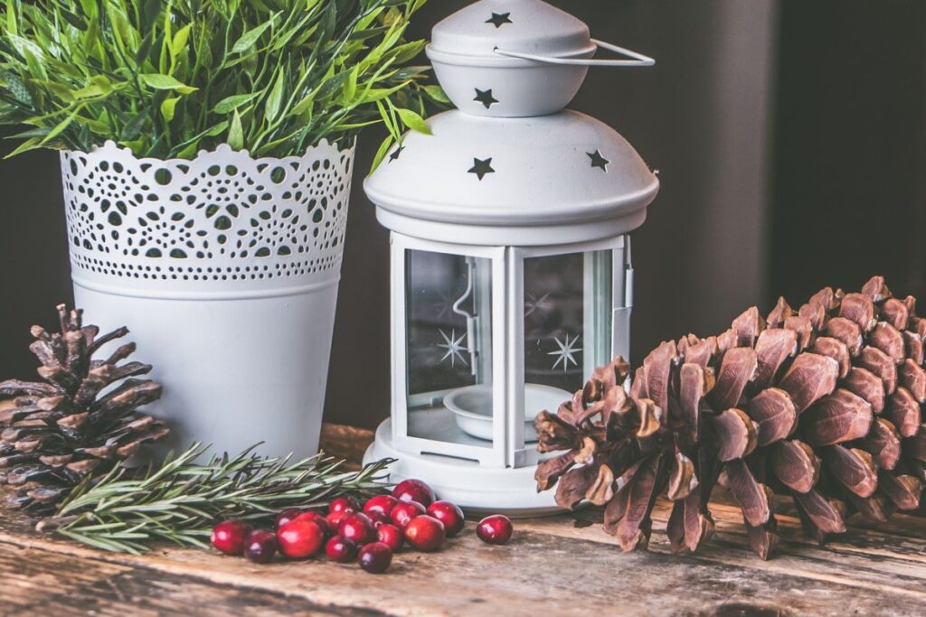 White candle lantern beside pinecones, red berries and greenery