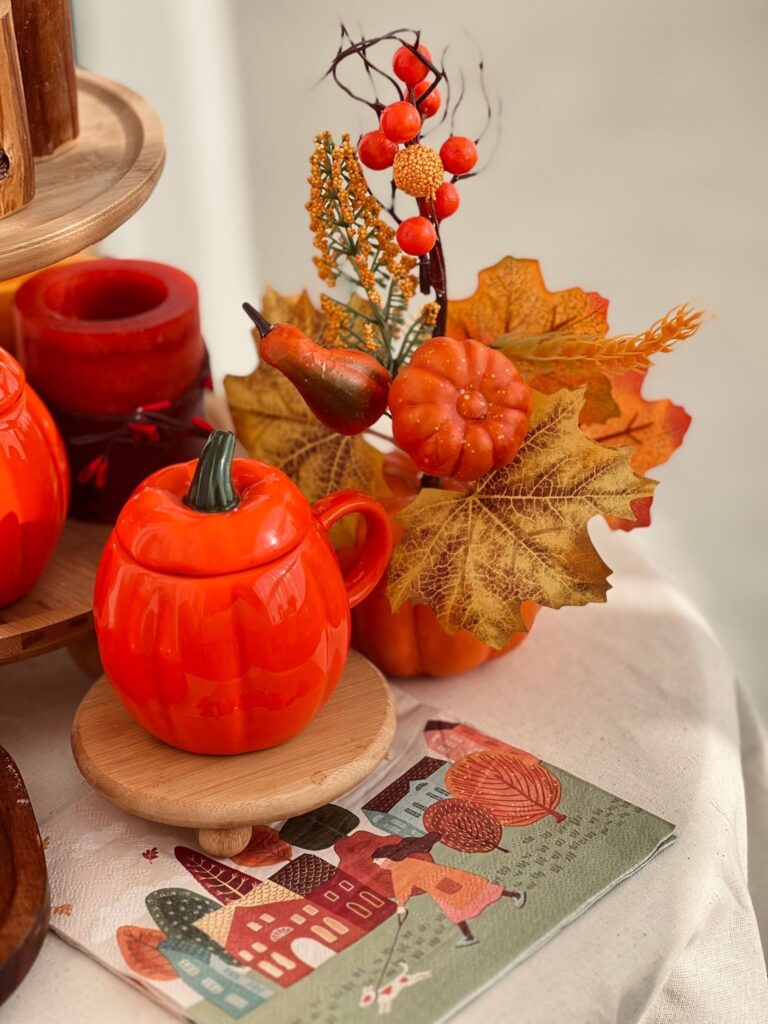 Autumn table with an orange pumpkin teapot, red berries and fall leaves