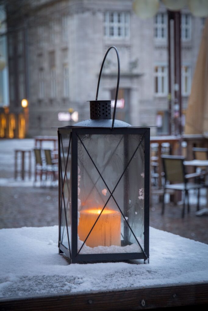 Black metal lantern with a lit candle on a snowy table