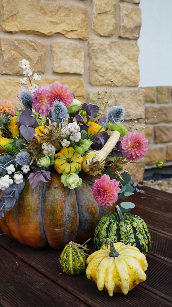 Fall flowers arranged inside a pumpkin with gourds around it