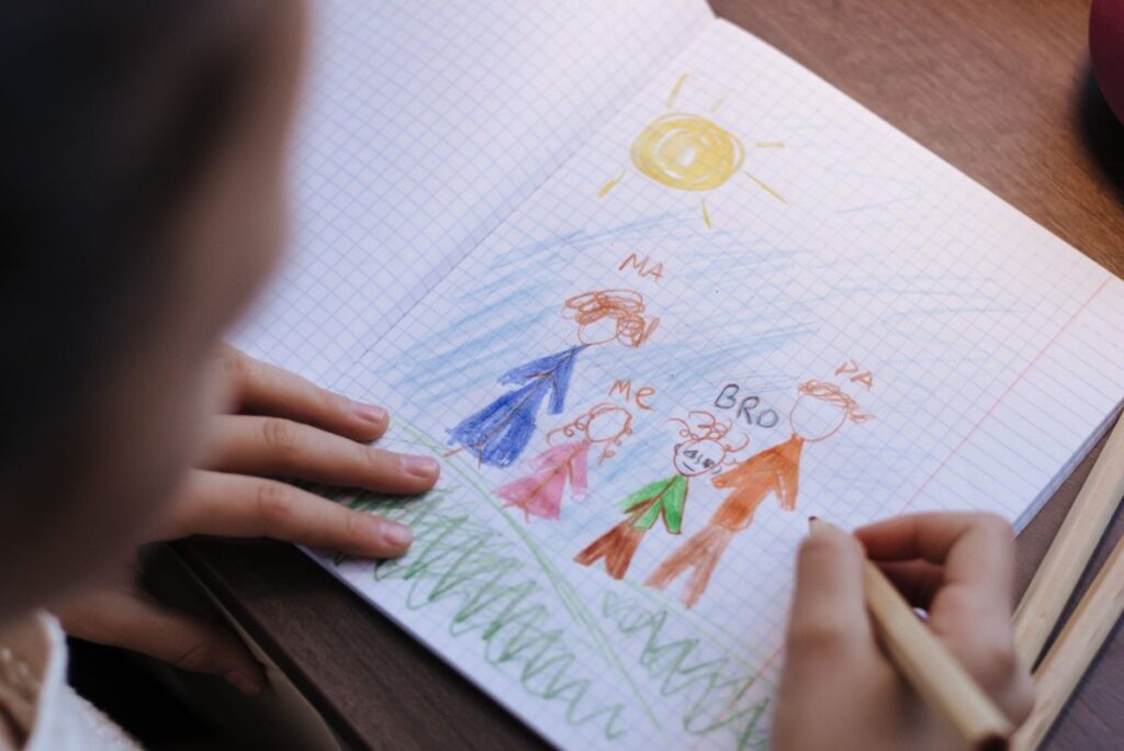Child drawing with crayons on paper at a wooden table