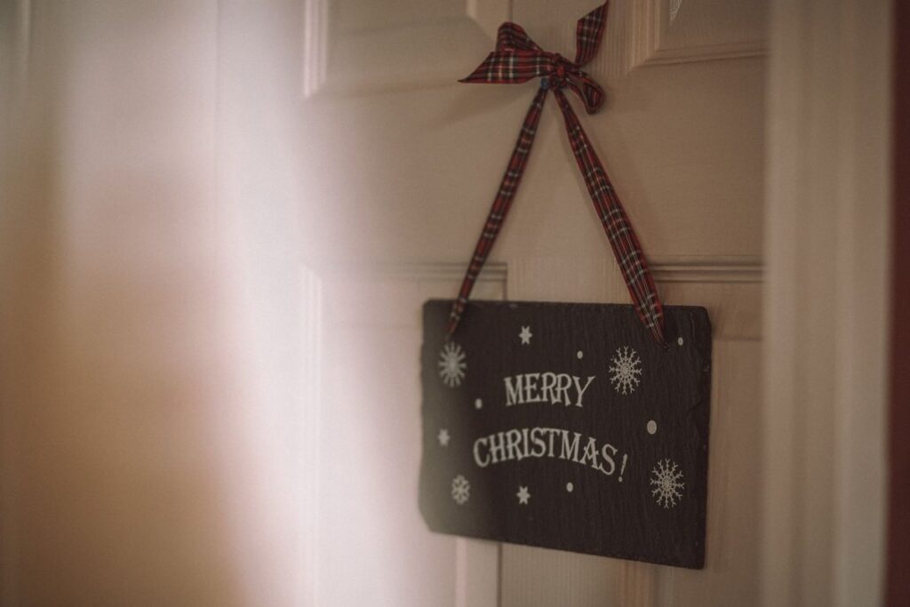 Merry Christmas sign hanging on a door from a plaid ribbon