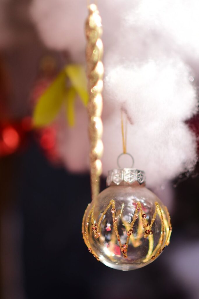 Clear glass ornament with gold detail hanging near a Christmas tree